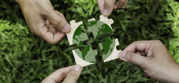 four people holding pieces of a jigsaw of the earth