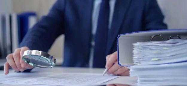 man with magnifying glass looking at documents